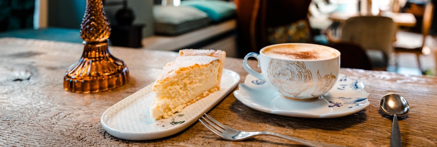 A piece of cake and a cup of coffee on a wooden table in a cozy café. Blurred furniture in the background., © SMG Stuttgart Marketing GmbH - Sarah Schmid