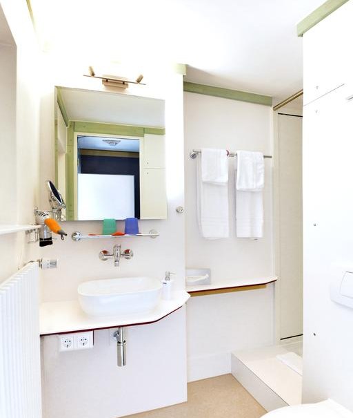 Helles Badezimmer mit Waschbecken, Spiegel, Handtüchern und Dusche. Minimalistisches Design mit weißen Wänden und grünen Akzenten., © Abalon Hotel Ideal Helles Badezimmer mit Waschbecken, Spiegel, Handtüchern und Dusche. Minimalistisches Design mit weißen Wänden und grünen Akzenten., © Abalon Hotel Ideal