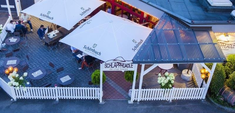 Terrasse mit weißen Sonnenschirmen und Holzmöbeln, umgeben von einem weißen Zaun. Menschen sitzen an Tischen, dekoriert mit Blumen., © Hotel Waldhorn Terrasse mit weißen Sonnenschirmen und Holzmöbeln, umgeben von einem weißen Zaun. Menschen sitzen an Tischen, dekoriert mit Blumen., © Hotel Waldhorn