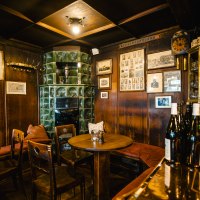 Gemütliche Weinstube mit Holzmöbeln, grünem Kachelofen, Bildern an den Wänden und Weinflaschen auf einem Tisch., © SMG Stuttgart Marketing GmbH - Sarah Schmid Gemütliche Weinstube mit Holzmöbeln, grünem Kachelofen, Bildern an den Wänden und Weinflaschen auf einem Tisch., © SMG Stuttgart Marketing GmbH - Sarah Schmid