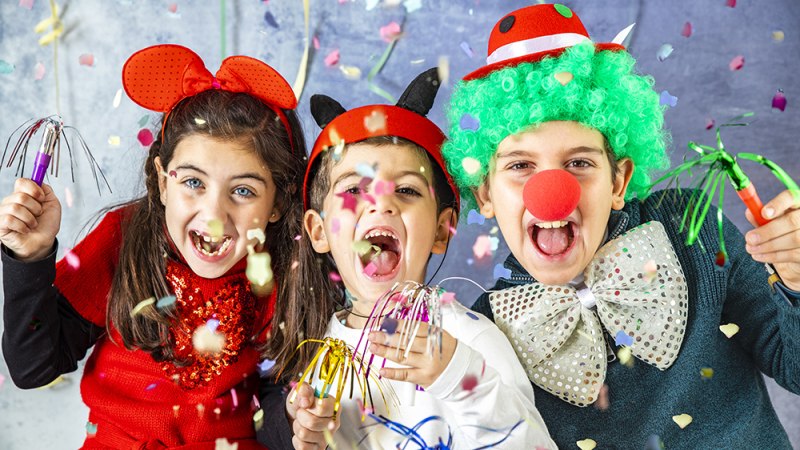 Drei fr&ouml;hliche Kinder in bunten Kost&uuml;men feiern Karneval mit Konfetti und Partyzubeh&ouml;r. Sie tragen lustige H&uuml;te und Accessoires., &copy; Getty Images/coscaron