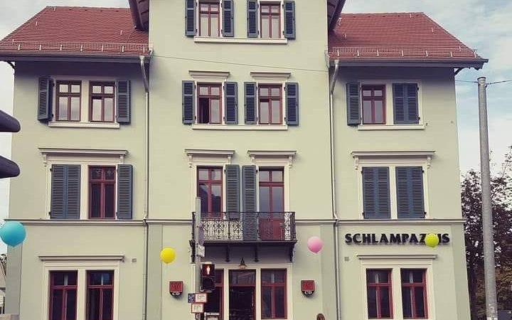 Dreist&ouml;ckiges Geb&auml;ude mit 'Schlampazius'-Schriftzug, bunten Luftballons und Menschen vor dem Eingang. Historische Architektur mit roten Fensterrahmen., &copy; Mora F&uuml;tterer