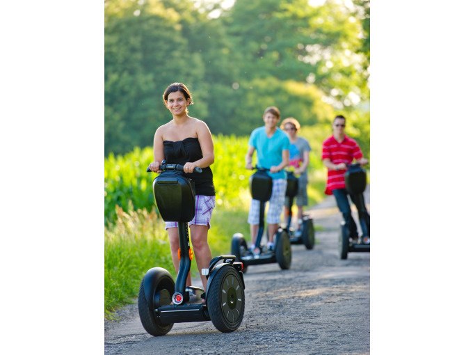 Four people on Segways ride along a rural path, surrounded by green nature and trees in the background., &copy; Cool-Tours StattReisen