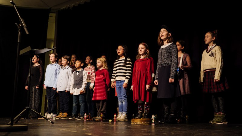 Ein Kinderchor steht auf einer Bühne und singt vor einem Mikrofon. Die Kinder tragen festliche Kleidung., © Foto: Thomas Neumayer