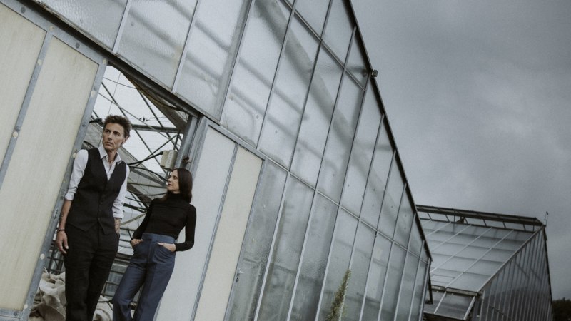 Zwei Personen stehen vor einem gro&szlig;en Gew&auml;chshaus. Der Himmel ist bew&ouml;lkt, und die Szene wirkt leicht melancholisch., &copy; Veranstalter