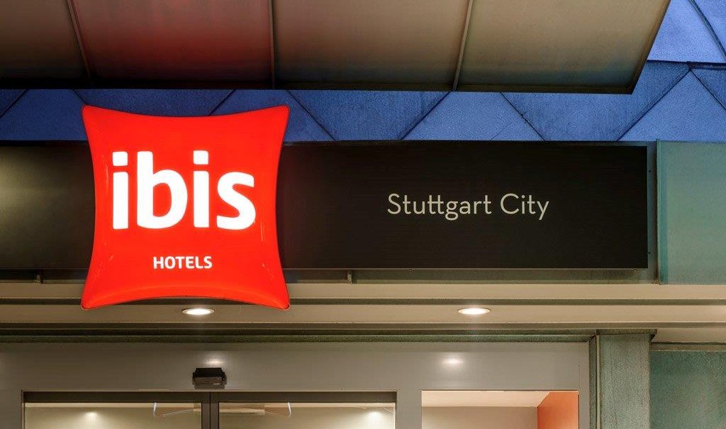 Eingang des Ibis Hotels in Stuttgart City mit leuchtendem roten Logo und schwarzem Schild., © TOMAS Eingang des Ibis Hotels in Stuttgart City mit leuchtendem roten Logo und schwarzem Schild., © TOMAS