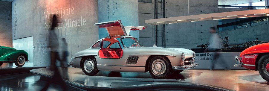 Silberner Oldtimer mit Flügeltüren im Mercedes-Benz Museum. Personen gehen vorbei, moderne Architektur im Hintergrund., © Mercedes-Benz Heritage GmbH