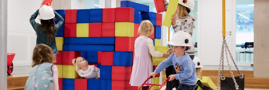 Children play on an indoor construction site with colorful foam blocks. They wear construction helmets and have fun building and playing., &copy; Julia Ochs