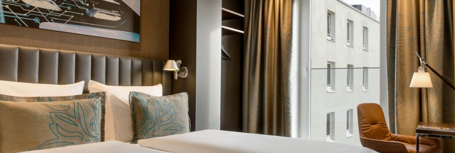 Modernes Hotelzimmer mit Doppelbett, Kunstwerk an der Wand, braunen Vorhängen und Fenster mit Blick auf ein Gebäude., © TOMAS Modernes Hotelzimmer mit Doppelbett, Kunstwerk an der Wand, braunen Vorhängen und Fenster mit Blick auf ein Gebäude., © TOMAS