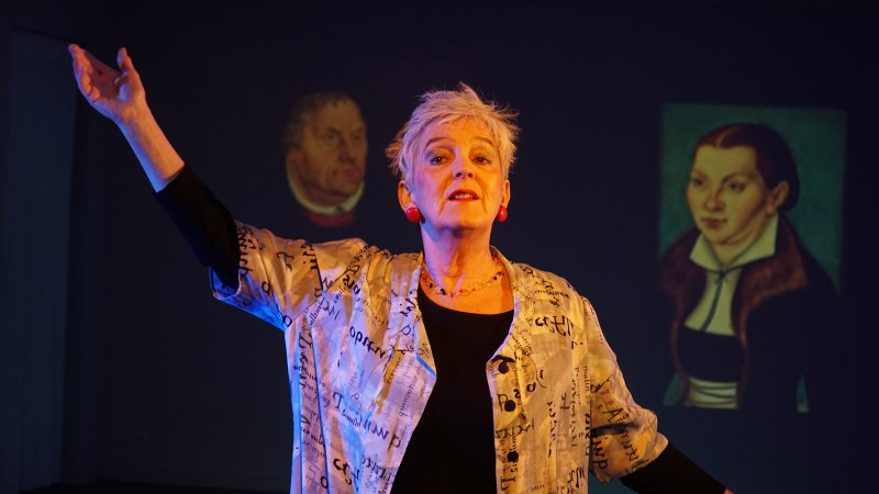 Eine Frau steht auf einer B&uuml;hne und gestikuliert. Im Hintergrund sind Projektionen von zwei historischen Portr&auml;ts zu sehen., &copy; Katja Ritter