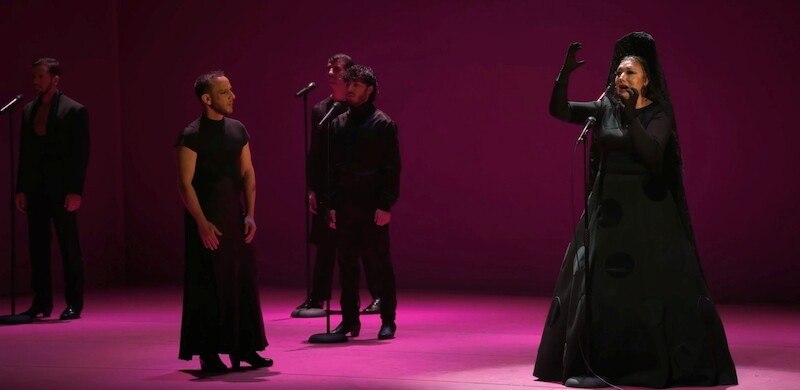 Flamenco-K&uuml;nstler auf einer B&uuml;hne in pinkem Licht. Eine Frau singt leidenschaftlich, w&auml;hrend andere K&uuml;nstler aufmerksam zuh&ouml;ren., &copy; Stuttgarter Flamenco Festival gUG