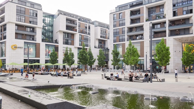 The Milaneo shopping center on Mail&auml;nder Platz with modern buildings, trees and a fountain in the foreground. People sit and walk., &copy; Peter Oppenl&auml;nder
