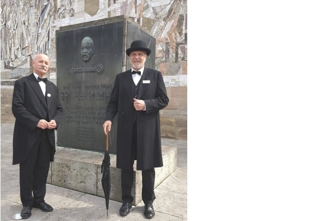 Zwei M&auml;nner in historischer Kleidung posieren vor einem Gottlieb-Daimler-Denkmal in Schorndorf. Sie tragen Anz&uuml;ge und H&uuml;te und halten Regenschirme., &copy; Eigenbetrieb Tourismus und Citymanagement Schorndorf