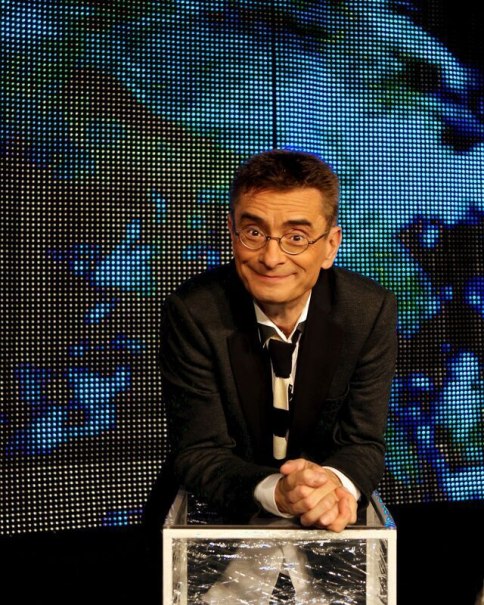 Ein Mann mit Brille und Anzug lehnt sich lächelnd auf einen durchsichtigen Würfel vor einem bunten, digitalen Hintergrund., © SKS Michael Russ GmbH