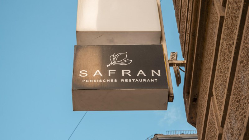 Schild eines persischen Restaurants namens Safran an einer Hauswand, vor blauem Himmel., © SMG, Sarah Schmid Schild eines persischen Restaurants namens Safran an einer Hauswand, vor blauem Himmel., © SMG, Sarah Schmid