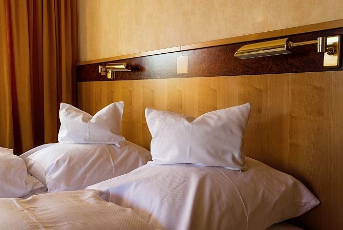 Zwei Betten mit weißen Kissen und Decken, Holzkopfteil und Leselampen in einem Gästezimmer., © Gästehaus Schlegel