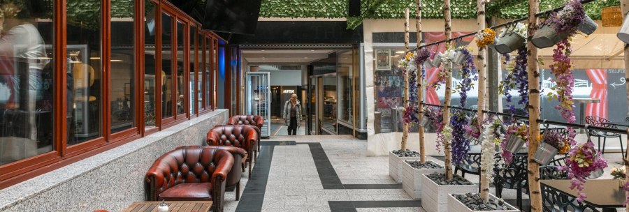 A cozy courtyard with red leather armchairs, decorative plants and a glass roof. A person enters the area in the background., &copy; SMG Stuttgart Marketing GmbH - Sarah Schmid