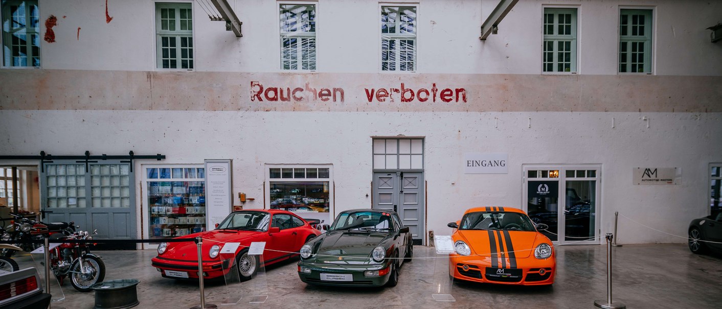 Drei Sportwagen stehen vor einer weißen Wand mit dem Schriftzug 'Rauchen verboten'. Links ein rotes, mittig ein grünes und rechts ein orangefarbenes Auto., © Stuttgart-Marketing GmbH, Thomas Niedermüller