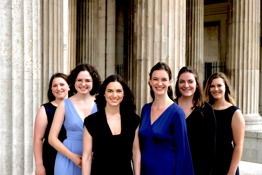 Sechs Frauen in eleganter Kleidung stehen vor beeindruckenden Säulen und lächeln in die Kamera. Sie wirken harmonisch und selbstbewusst., © Luminosa Frauenvokalensemble Sechs Frauen in eleganter Kleidung stehen vor beeindruckenden Säulen und lächeln in die Kamera. Sie wirken harmonisch und selbstbewusst., © Luminosa Frauenvokalensemble