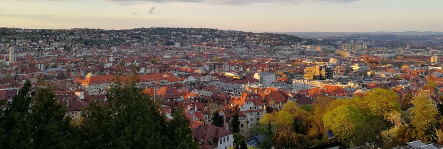 Panoramic view of Stuttgart at sunset, with red roofs and green trees in the foreground. The sky is slightly cloudy., © Stuttgart-Marketing GmbH Panoramic view of Stuttgart at sunset, with red roofs and green trees in the foreground. The sky is slightly cloudy., © Stuttgart-Marketing GmbH
