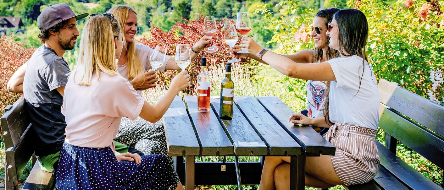 Five people clink glasses of wine at a wooden table outside, surrounded by greenery and flowers., &copy; SMG, Thomas Niederm&uuml;ller