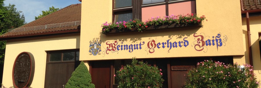 Gelbes Gebäude mit der Aufschrift 'Weingut Gerhard Zaiß', umgeben von Blumen und Pflanzen., © Simone Mack Gelbes Gebäude mit der Aufschrift 'Weingut Gerhard Zaiß', umgeben von Blumen und Pflanzen., © Simone Mack