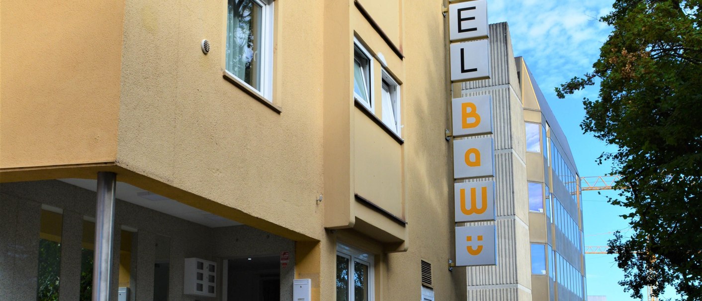 Gelbes Hotelgebäude mit Schild 'Hotel BaWü', Treppe zum Eingang, umgeben von Bäumen und modernen Gebäuden im Hintergrund., © Hotel BaWü Gelbes Hotelgebäude mit Schild 'Hotel BaWü', Treppe zum Eingang, umgeben von Bäumen und modernen Gebäuden im Hintergrund., © Hotel BaWü