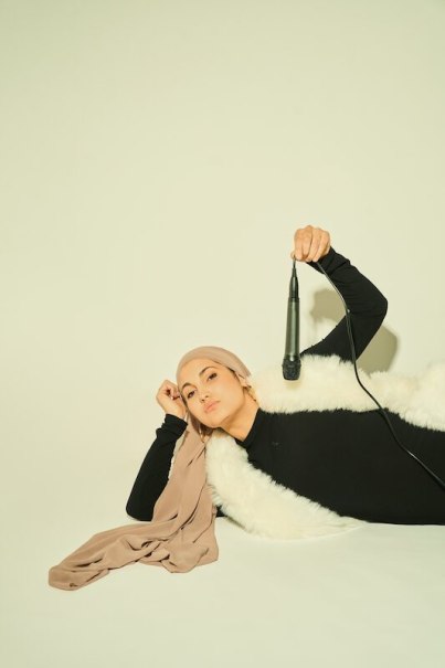 Person is lying on the floor, holding a microphone, wearing a light-colored scarf and black clothing., © Rosenau Kultur e.V. Person is lying on the floor, holding a microphone, wearing a light-colored scarf and black clothing., © Rosenau Kultur e.V.