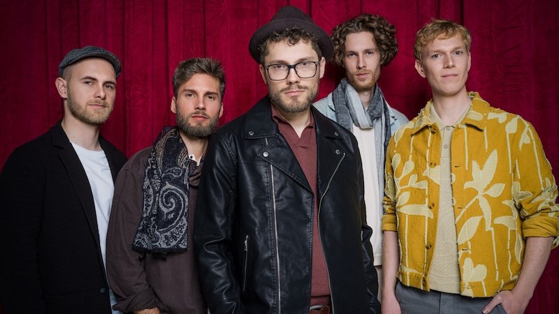 Fünf Männer stehen vor einem roten Vorhang. Sie tragen verschiedene modische Outfits, darunter Lederjacke, Schal und gemusterte Jacke., © Theaterhaus Stuttgart e.V. Fünf Männer stehen vor einem roten Vorhang. Sie tragen verschiedene modische Outfits, darunter Lederjacke, Schal und gemusterte Jacke., © Theaterhaus Stuttgart e.V.