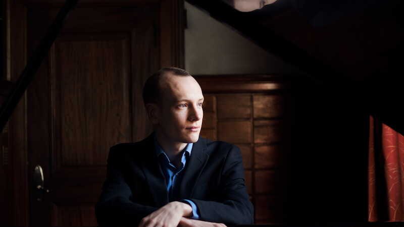 Orchester in formeller Kleidung posiert auf Treppe vor klassischem Geb&auml;ude. Musiker halten Instrumente, tragen rote und schwarze Outfits., &copy; Klassische Philharmonie Bonn e.V.