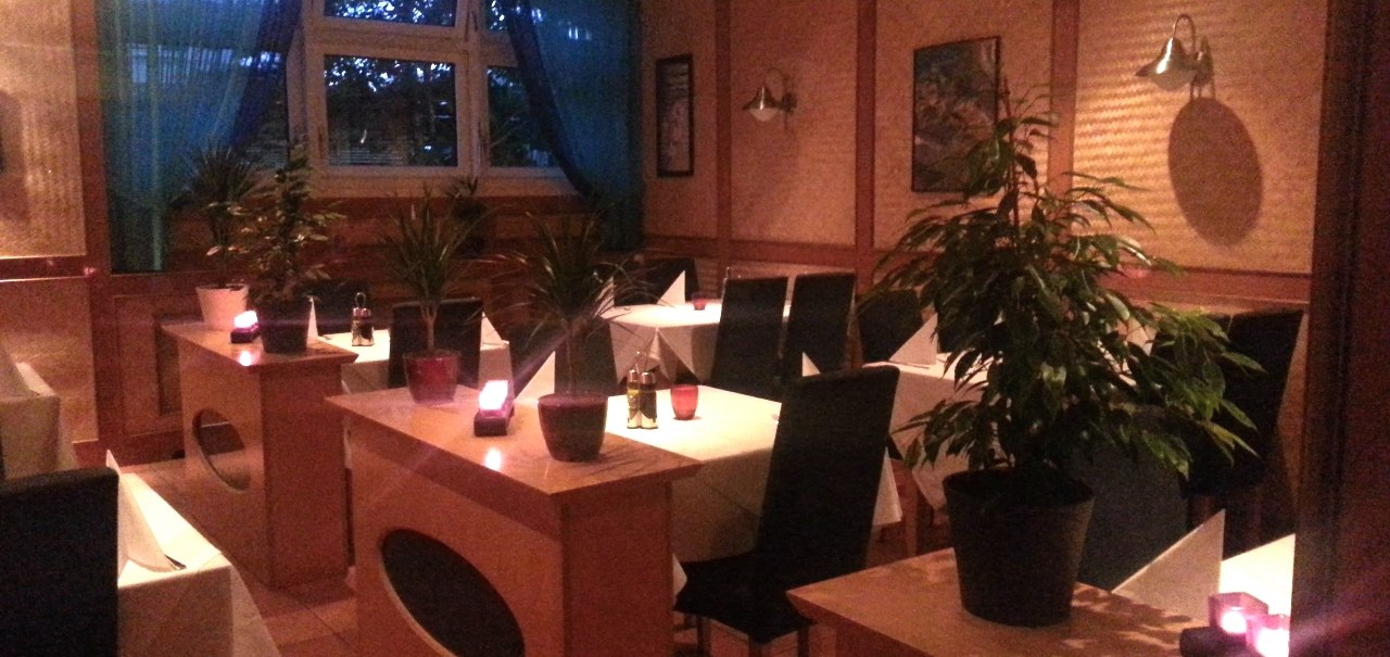 Ein gem&uuml;tliches Restaurant mit Kerzenlicht, Pflanzen und gedeckten Tischen. Dunkle St&uuml;hle und blaue Vorh&auml;nge schaffen eine einladende Atmosph&auml;re., &copy; Restaurant Akropolis