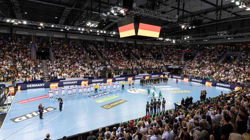 Handball-Länderspiel in einer vollen Arena. Zwei Mannschaften stehen auf dem Spielfeld, während die Zuschauer die Nationalhymne hören., © Kenny Beele Handball-Länderspiel in einer vollen Arena. Zwei Mannschaften stehen auf dem Spielfeld, während die Zuschauer die Nationalhymne hören., © Kenny Beele