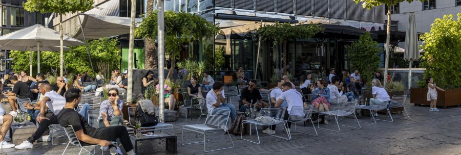 People relax in a lively outdoor caf&eacute;, surrounded by plants and modern buildings. A sign prohibits skateboarding., &copy; SMG, Sarah Schmid