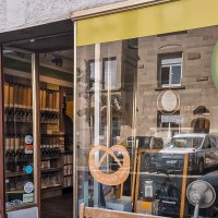 Exterior view of an unpackaged store with a bulk goods logo. Containers with food and a sign with "BIO" can be seen in the shop window., © Schüttgut, Stuttgart Exterior view of an unpackaged store with a bulk goods logo. Containers with food and a sign with "BIO" can be seen in the shop window., © Schüttgut, Stuttgart