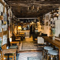 Ein gemütliches Café mit Holzmöbeln, Bücherregalen und Dekorationen an den Wänden. Einladende Atmosphäre mit warmem Licht., © Café Che