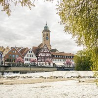 A view of N&uuml;rtingen with half-timbered houses and a church tower by the river. Flowering trees and a fish ladder in the foreground., &copy; SMG Stuttgart Marketing GmbH - Sarah Schmid