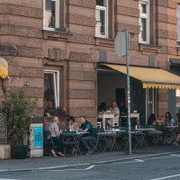 Café mit gelbem Vordach an einer Straßenecke. Gäste sitzen draußen an Tischen. Schild mit 'Lumen' und Straßenschild 'Schwabstr.' sichtbar., © SMG, Sarah Schmid Café mit gelbem Vordach an einer Straßenecke. Gäste sitzen draußen an Tischen. Schild mit 'Lumen' und Straßenschild 'Schwabstr.' sichtbar., © SMG, Sarah Schmid