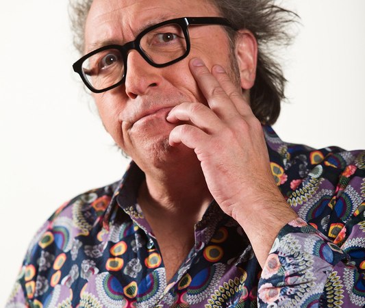 A man with tousled hair and a colorful shirt looks thoughtful. He wears glasses and supports his chin with his hand., &copy; Theaterhaus Stuttgart e.V.