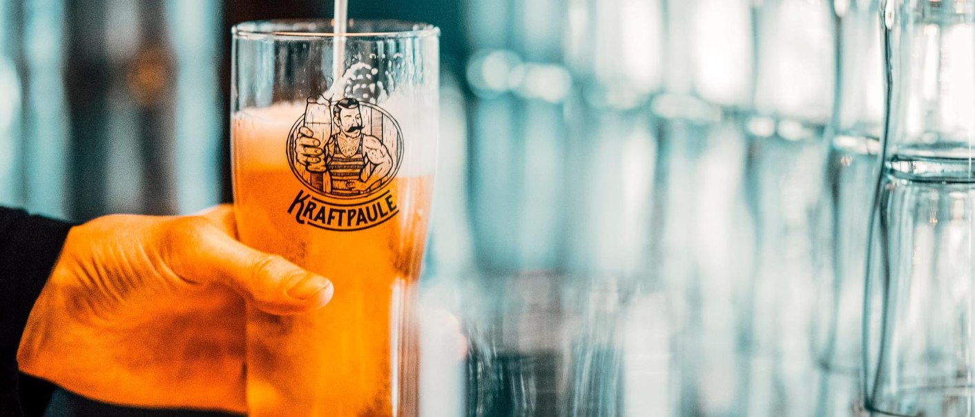 Ein Glas mit dem Logo von Kraftpaule wird mit Bier gef&uuml;llt. Im Hintergrund sind unscharfe Gl&auml;ser zu sehen., &copy; Kraftpaule, Stuttgart