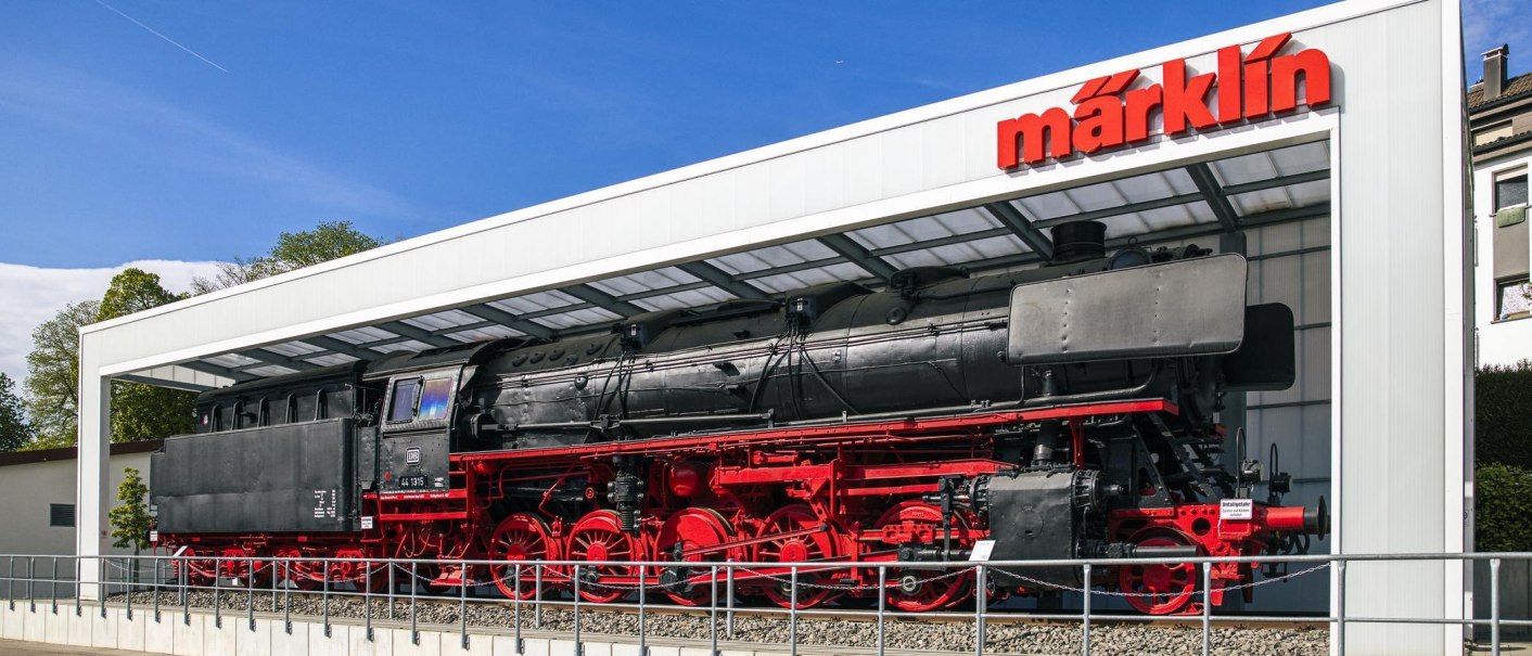 A black steam locomotive with red wheels stands in front of the Märklineum in Göppingen under a modern glass roof., © SMG Stuttgart Marketing GmbH - Sarah Schmid A black steam locomotive with red wheels stands in front of the Märklineum in Göppingen under a modern glass roof., © SMG Stuttgart Marketing GmbH - Sarah Schmid
