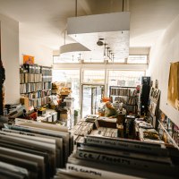 Ein gemütlicher Plattenladen voller Schallplatten. Ein Mann sitzt an einem Schreibtisch, umgeben von Regalen und Postern an den Wänden., © SMG Stuttgart Marketing GmbH - Sarah Schmid Ein gemütlicher Plattenladen voller Schallplatten. Ein Mann sitzt an einem Schreibtisch, umgeben von Regalen und Postern an den Wänden., © SMG Stuttgart Marketing GmbH - Sarah Schmid