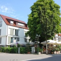 Modern and traditional buildings on a street corner, with a large tree and a caf&eacute; with umbrellas., &copy; Jeanette Bender
