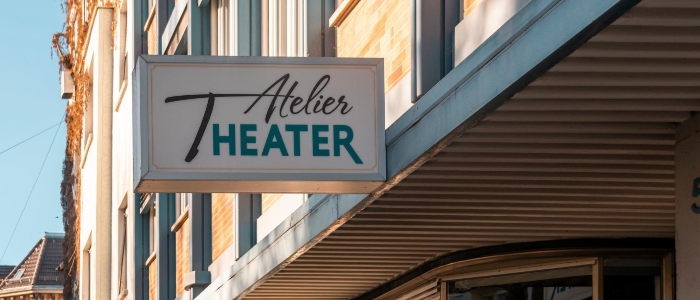 Ein Schild mit der Aufschrift 'Atelier Theater' hängt an einem Gebäude. Die Fassade ist modern und das Wetter ist sonnig., © SMG, Sarah Schmid Ein Schild mit der Aufschrift 'Atelier Theater' hängt an einem Gebäude. Die Fassade ist modern und das Wetter ist sonnig., © SMG, Sarah Schmid