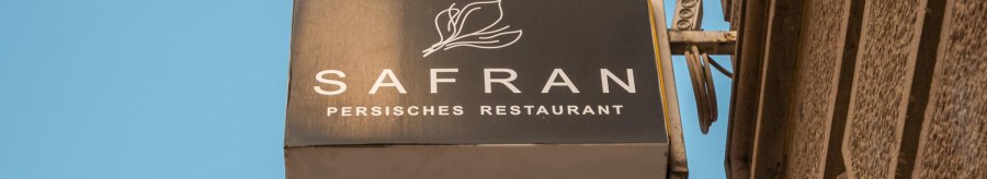 Sign of a Persian restaurant called Safran on a house wall, against a blue sky., © SMG Stuttgart Marketing GmbH - Sarah Schmid