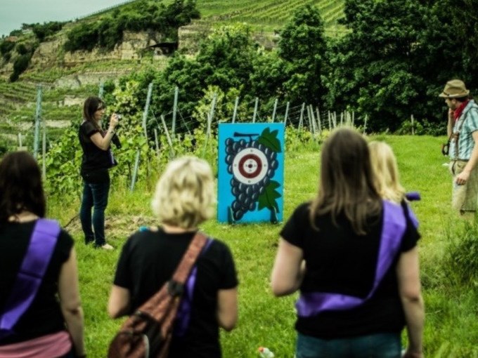 People in a vineyard on a wine safari, with a target in the shape of a bunch of grapes. Vines and hills can be seen in the background., © Cool-Tours StattReisen People in a vineyard on a wine safari, with a target in the shape of a bunch of grapes. Vines and hills can be seen in the background., © Cool-Tours StattReisen