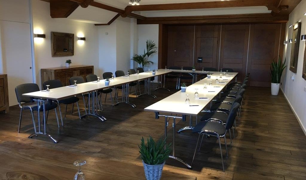 Modern meeting room with U-shaped table arrangement, chairs, wooden floor and plants. Subtle lighting and wooden elements on the ceiling., © TOMAS