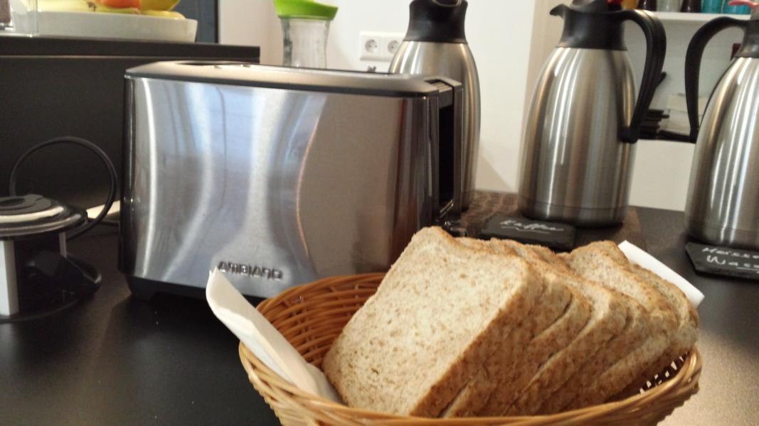 Ein Toaster steht neben einem Korb mit Brotscheiben. Im Hintergrund sind mehrere Thermoskannen zu sehen., © TOMAS Ein Toaster steht neben einem Korb mit Brotscheiben. Im Hintergrund sind mehrere Thermoskannen zu sehen., © TOMAS