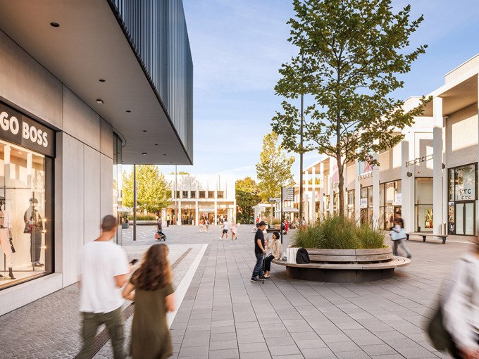 Einkaufsstraße in der Outletcity Metzingen mit Geschäften, Passanten und einem Baum in der Mitte., © Schlienz-Tours GmbH & Co.KG Einkaufsstraße in der Outletcity Metzingen mit Geschäften, Passanten und einem Baum in der Mitte., © Schlienz-Tours GmbH & Co.KG