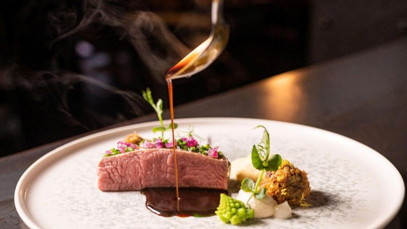 Ein kunstvoll angerichtetes Gourmetgericht mit Fleisch, Gemüse und einer dunklen Sauce, die aus einer Kelle auf den Teller gegossen wird., © 5 - Stuttgart