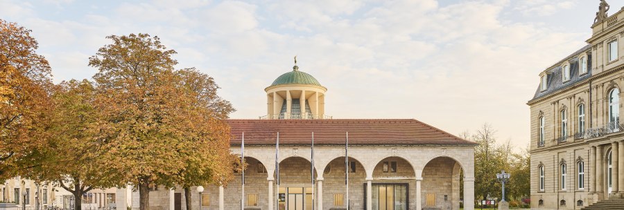 Historisches Gebäude mit Kuppel und Bögen, umgeben von herbstlichen Bäumen und gepflegtem Rasen., © Simon Sommer